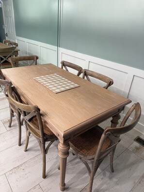 A dining table with six wooden chairs, a chessboard, and a white door in the background.