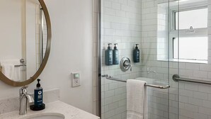 Ein Badezimmer mit rundem Spiegel, Waschbecken, Duschkabine aus Glas und Pflegeprodukten an der Wand.