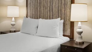 Ein Hotelzimmer mit einem Bett, zwei Nachttischlampen, einem hölzernen Kopfteil und einem dunkelbraunen Aktenschrank.