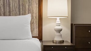 Ein Bett mit zwei Kissen, ein Nachttisch mit Lampe und ein Holz-Kopfteil.