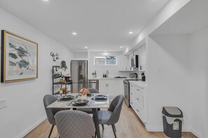 Une cuisine moderne avec des meubles blancs, un réfrigérateur en acier inoxydable et un coin repas avec une table dressée pour deux personnes.