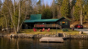 En stuga med ett grönt tak, en brygga och röda Adirondack-stolar vid en sjö.