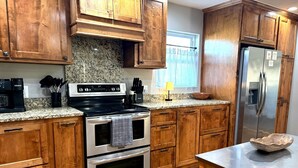 Una cocina con armarios de madera, un refrigerador de acero inoxidable, horno empotrado y encimera de granito.