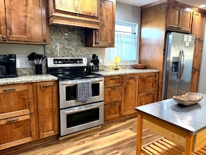 A kitchen with wooden cabinets, a stainless steel refrigerator, a built-in oven, and a granite countertop. - Bike to Coler - Private Backyard - Big Kitchen:  The Roost - Bentonville, AR (Bentonville)