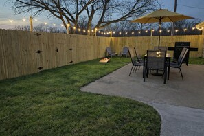 A backyard with a wooden fence, a concrete patio, and a table with chairs. - Bike to Coler - Private Backyard - Big Kitchen:  The Roost - Bentonville, AR (Bentonville)