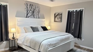 Un dormitorio con una cama blanca, dos mesitas de noche con lámparas, un ventilador de techo y obras de arte en las paredes.