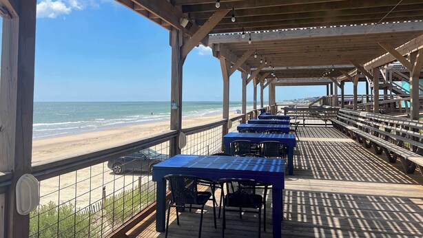 Eine Terrass mit Tischen und Stühlen mit Blick auf einen Strand.