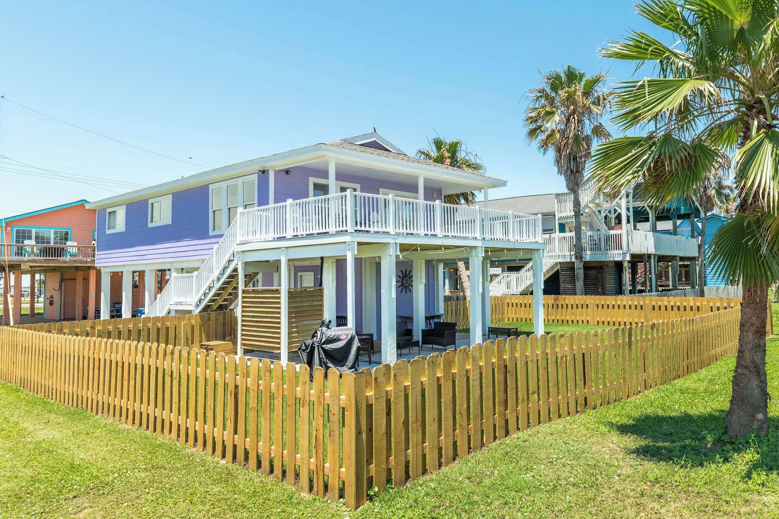 A two-story house with a balcony, a wooden fence, and a palm tree.