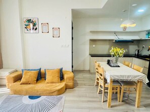 Ein modernes Wohnzimmer mit Sofa, einem Esstisch mit Stühlen, einer Küchenzeile inklusive Herd und einer hängenden Leuchte.