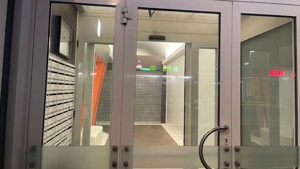 Un interior moderno con una puerta de vidrio, manijas de metal y un pasillo visible con una persiana cerrada.