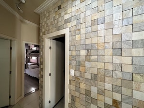A hallway with a tiled wall, a door leading to a room with a bed, and a light switch on the wall. - Complete and cozy house for 7 people. (Maringá)