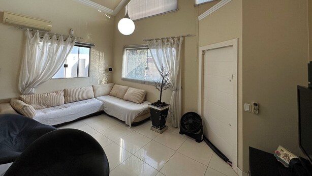Uma sala de estar com um sofá seccional, uma planta em vaso, um ventilador e uma televisão.