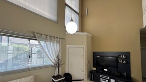 Uma sala de estar com um sofá, uma televisão sobre um suporte preto, uma planta em vaso e uma porta.