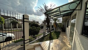 Uma entrada com portão, um pátio com azulejos, uma galeria coberta e vista para a rua.