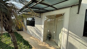Uma área externa coberta com porta de vidro, piso de azulejos e uma palmeira.