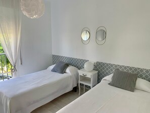 Ein Hotelzimmer mit zwei Betten, einem kleinen Nachttisch, einem Spiegel und einem Fenster mit Vorhängen.