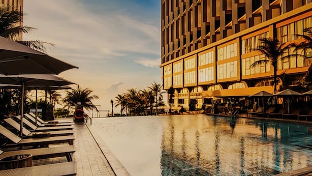 A hotel pool area with lounge chairs and umbrellas, surrounded by tall buildings. - The Trinity Mandala Seaview (Mui Ne)