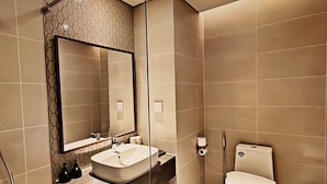 A modern bathroom with a large mirror, a sink, a toilet, and a shower area. - The Trinity Mandala Seaview (Mui Ne)