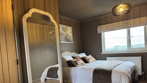 Un dormitorio con un espejo grande, una cama con muchas almohadas, un radiador y una ventana con vistas.
