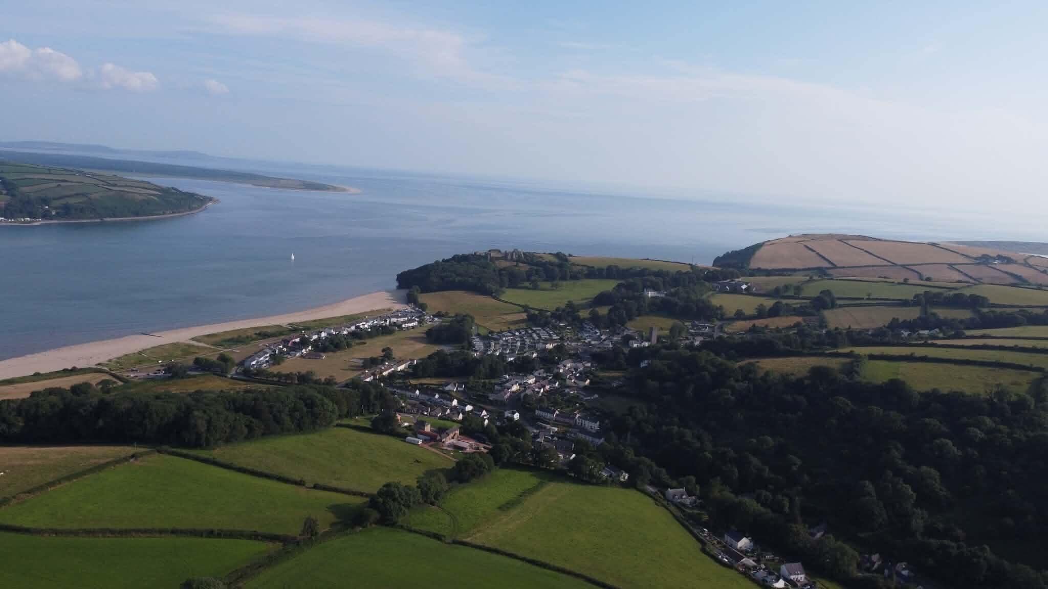 An aerial view of a coastal village with fields, a beach, and a small town.