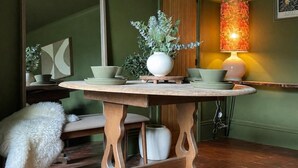 Un comedor con una mesa de madera redonda, un espejo, un jarrón con plantas y un perro.