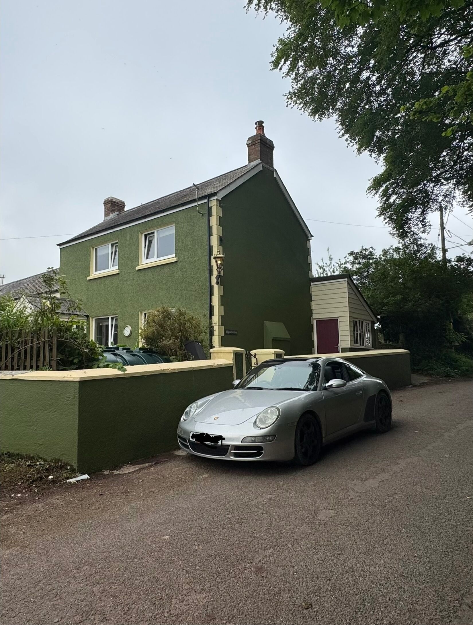 A residential building with a green facade, a driveway, and a parked silver sports car.
