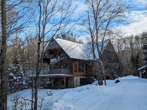 A cabin with a large deck, surrounded by snow-covered trees.