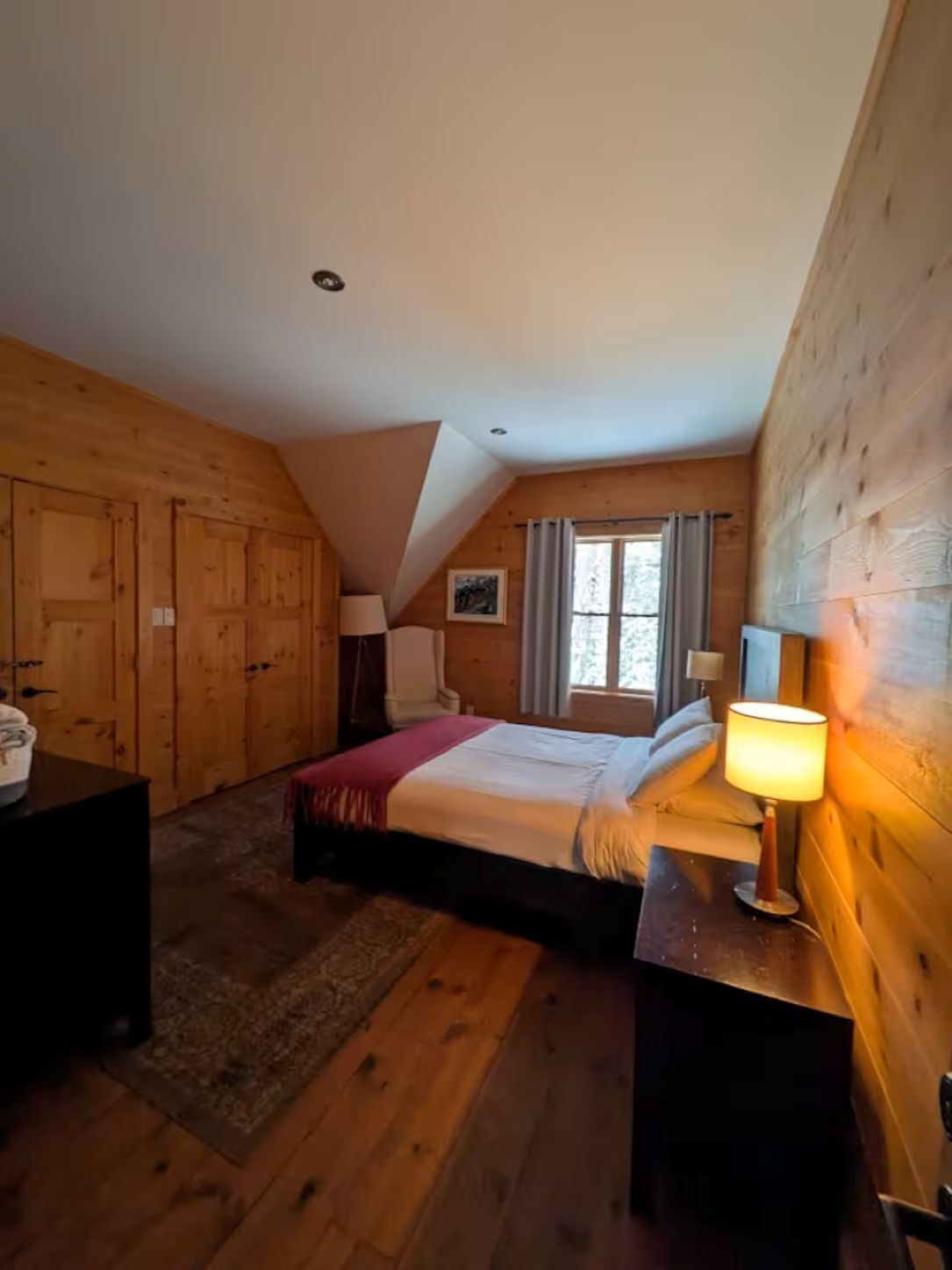 Una habitación de madera con una cama, un escritorio y una ventana.
