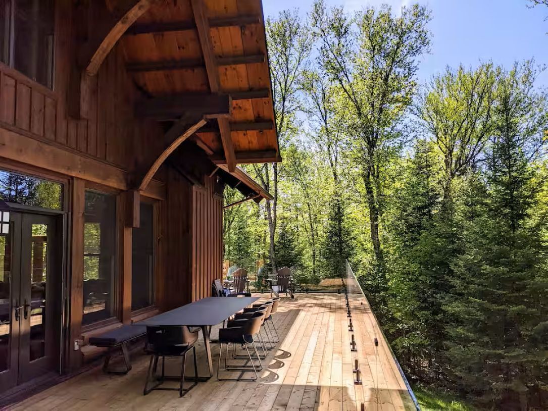 A wooden deck with a dining table and chairs, surrounded by forest.