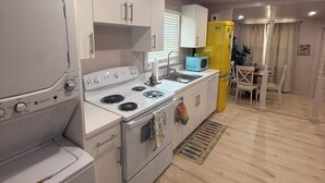 Una cocina compacta con electrodomésticos blancos, un refrigerador amarillo y un comedor con mesa y sillas.