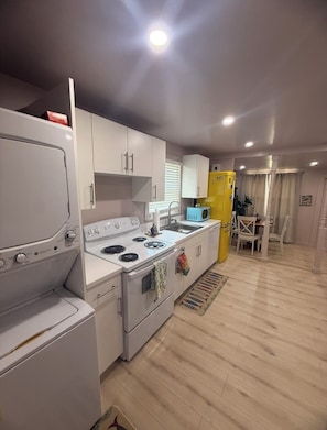 A compact kitchen with white appliances, a yellow refrigerator, and a dining area with a table and chairs. - The Lil Pink House: Walkable to Downtown Gem w/ AC & Washer/Dryer (Jensen Beach)