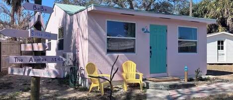A small pink building with a green door, two yellow chairs outside, and directional signs.