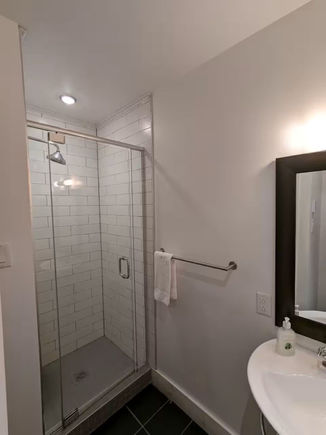 A bathroom with a glass shower enclosure, a white sink with a mirror, and a towel rack.