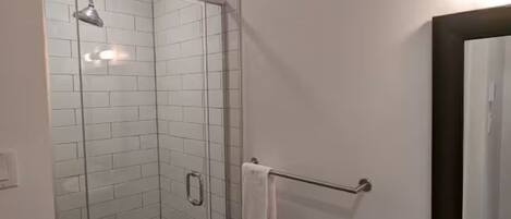 A bathroom with a glass shower enclosure, a white sink with a mirror, and a towel rack.