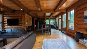 A log cabin interior with a living area, sofa, dining table, and large windows. - Spacious family 5 Bedroom Chalet, Hot Tub, pet-friendly, pool lake tennis (Lac-Supérieur)