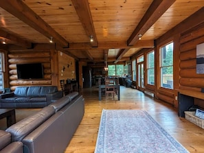A log cabin interior with a living area, sofa, dining table, and large windows.