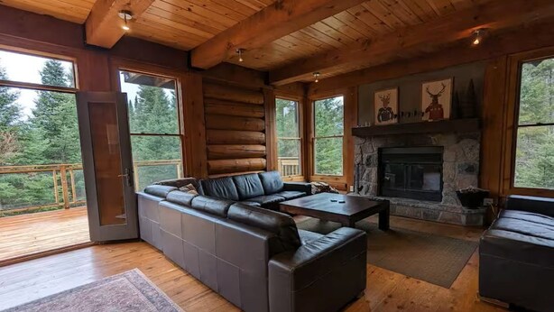 A log cabin interior with a sectional sofa, fireplace, and large windows. - Spacious family 5 Bedroom Chalet, Hot Tub, pet-friendly, pool lake tennis (Lac-Supérieur)