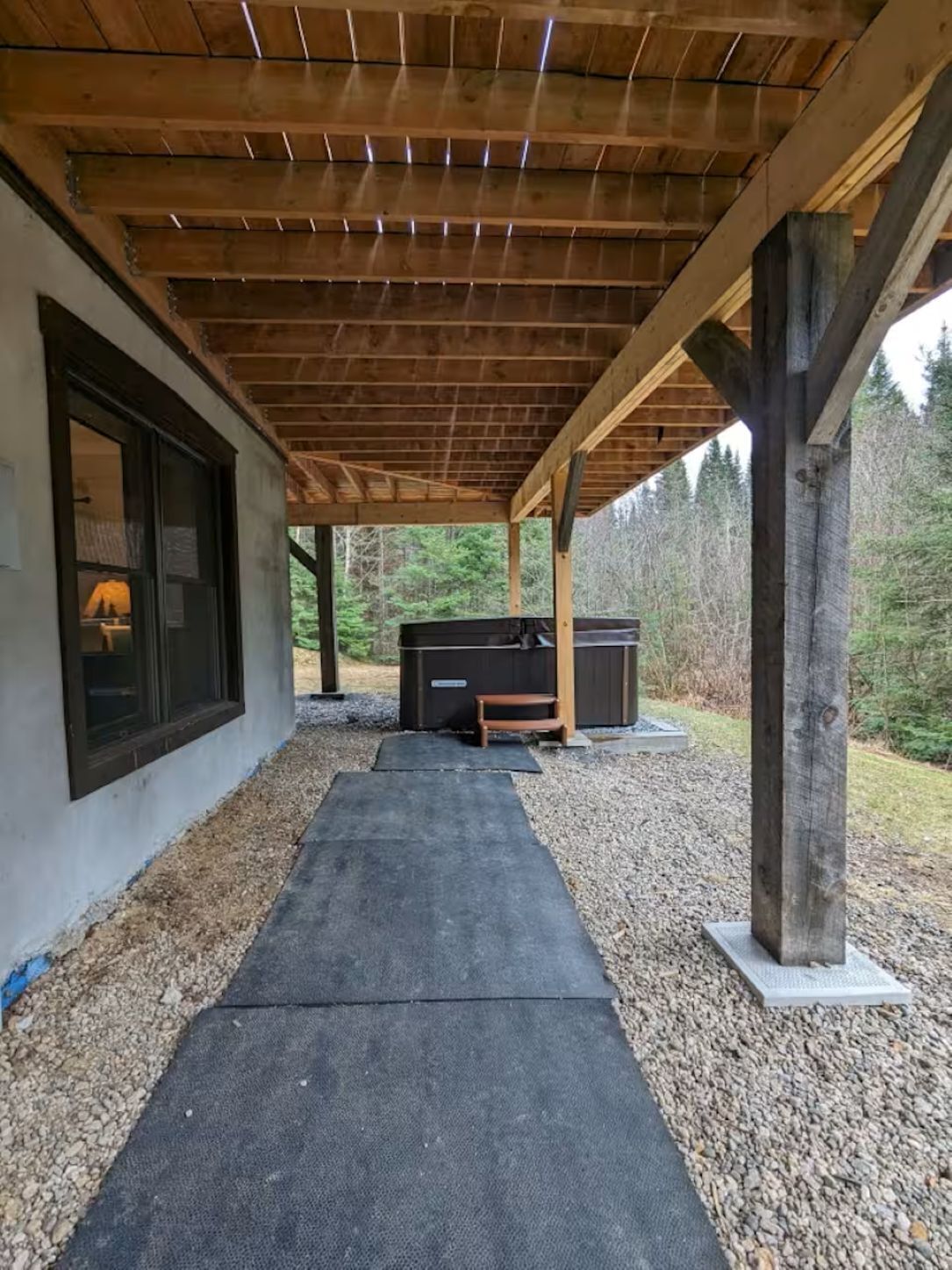 Un espace extérieur abrité, doté d’un chemin en béton, de poutres en bois et d’un jacuzzi.