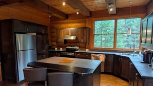 A modern kitchen with wooden cabinetry, a stainless steel refrigerator, and a large island with chairs. - Spacious family 5 Bedroom Chalet, Hot Tub, pet-friendly, pool lake tennis (Lac-Supérieur)