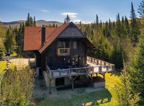 A log cabin with a balcony, surrounded by forest.