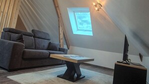 Ein gemütliches Schlafzimmer im Dachgeschoss mit geneigter Decke, einer Couch, einem Couchtisch, einem kleinen Beistelltisch und einem Dachfenster.