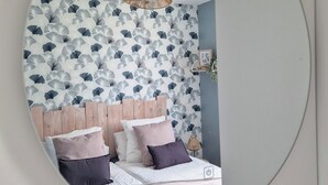 Ein Schlafzimmer mit einem runden Spiegel, einem Bett mit vielen Kissen, einem Holz-Kopfteil und einer Wand mit einem floralen Tapetenmuster.