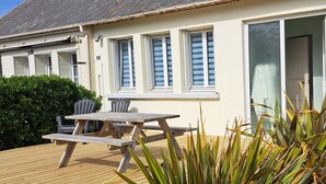 Ein Haus mit einer Holzterrasse, einem Patio-Tisch, zwei Stühlen und einem Blumentopf.