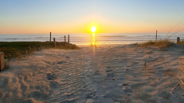 Ein Strand mit einem Zaun, Fußspuren und blauem Himmel.