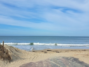 Ein Strand mit Holzzaun, sandigem Ufer und ruhigen Wellen.