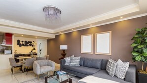 A modern living room with a grey sofa, a glass coffee table, and a dining area with a white table and chairs. - New Cumberland 405 by CTHA (Cape Town)
