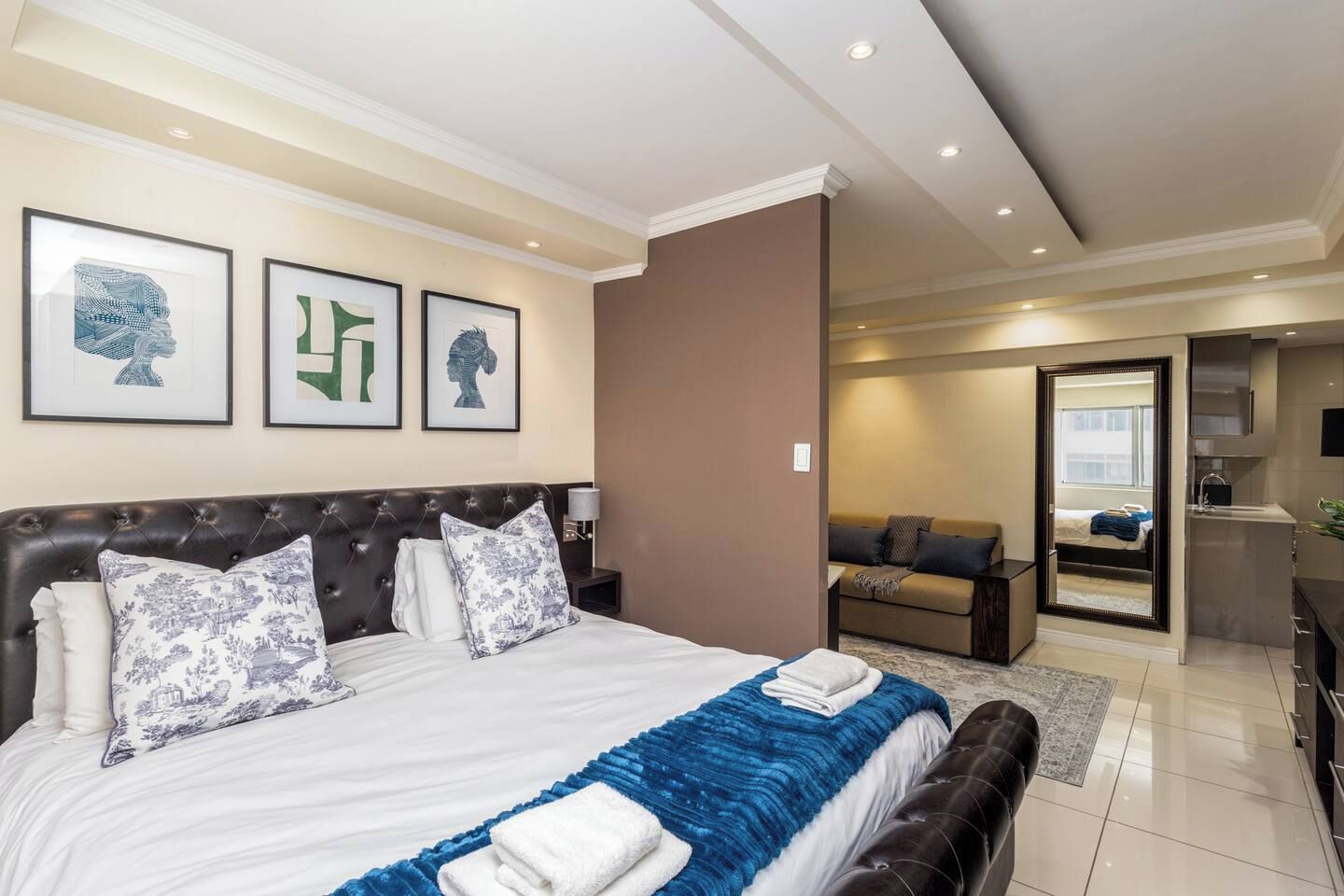 Une chambre d’hôtel avec un grand lit, un canapé, un miroir et une salle de bain visible à travers une porte ouverte.