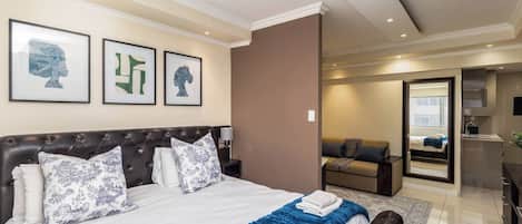 Une chambre d’hôtel avec un grand lit, un canapé, un miroir et une salle de bain visible à travers une porte ouverte.