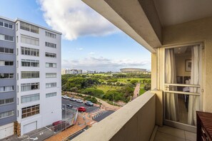 Een balkon met uitzicht op een stadsgezicht, inclusief een gebouw met meerdere ramen en een parkeerterrein.
