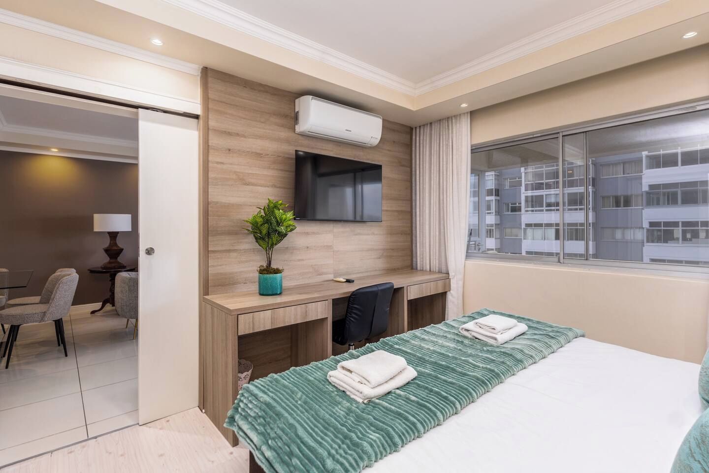 A hotel room with a bed, a desk, a chair, a TV, and a window with a city view.